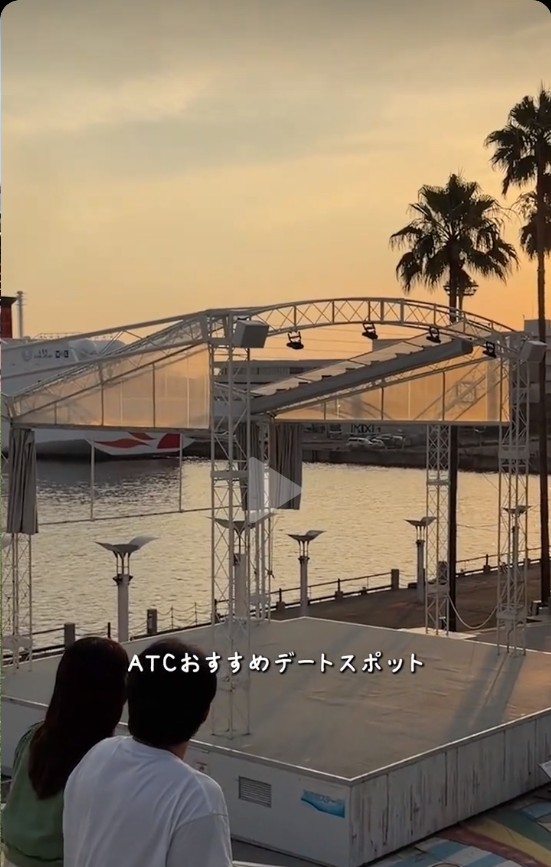 夕焼けの海辺のステージの前に並んで腰かけるふたり