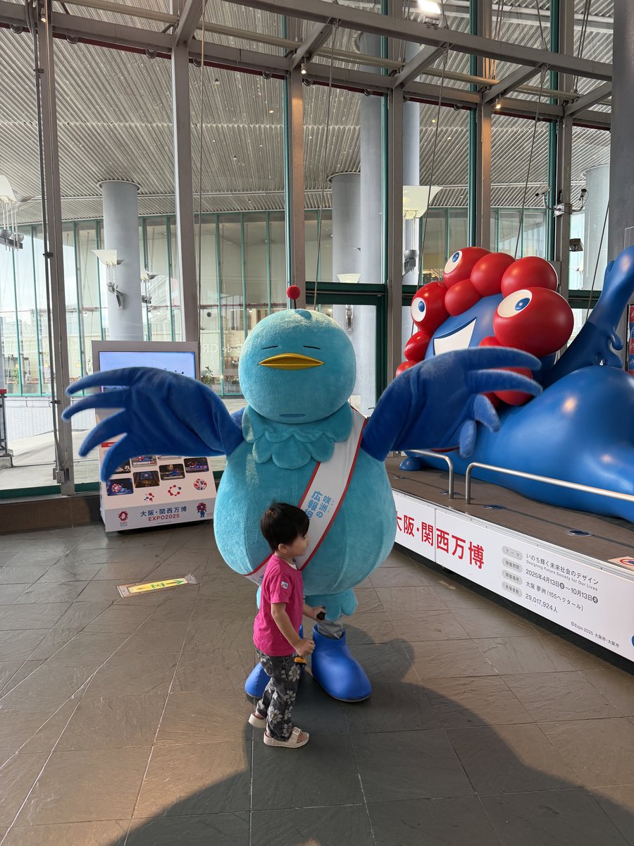 羽を広げたサキドリちゃんのそばに立つ、小さなお子さん
